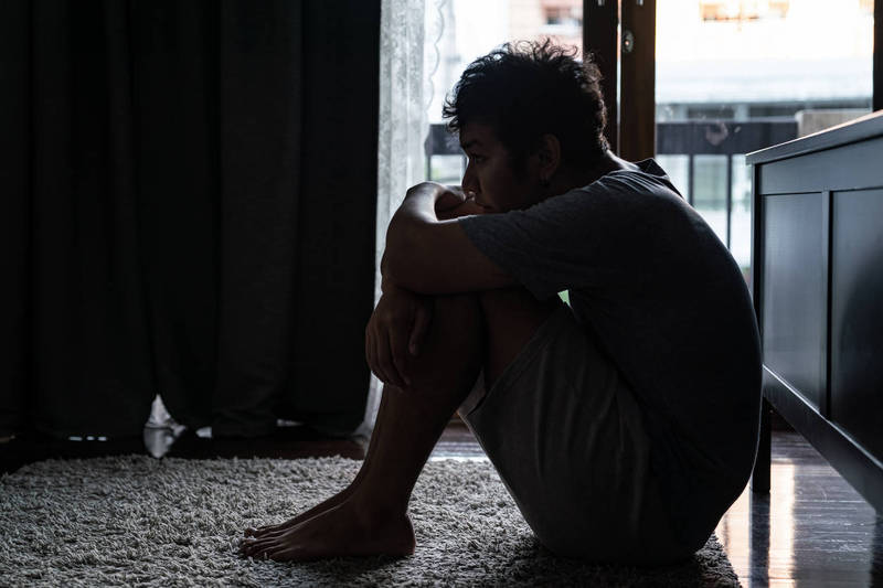 Wide shot of young adult asian loneliness sad man sitting on the floor in bedroom hugging the knees and cry. Broken heart despair man sitting on the floor and thinking alone."n