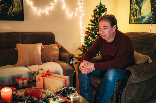 Senior caucasian man sitting on a couch and waiting alone for Christmas / New Year's eve.